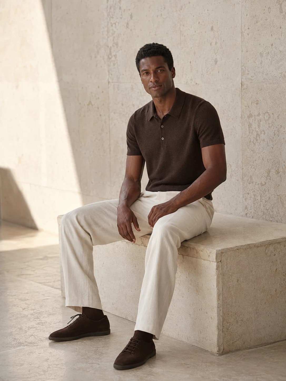 Illustrative menswear editorial: an AI model in a chocolate knit polo and ivory trousers